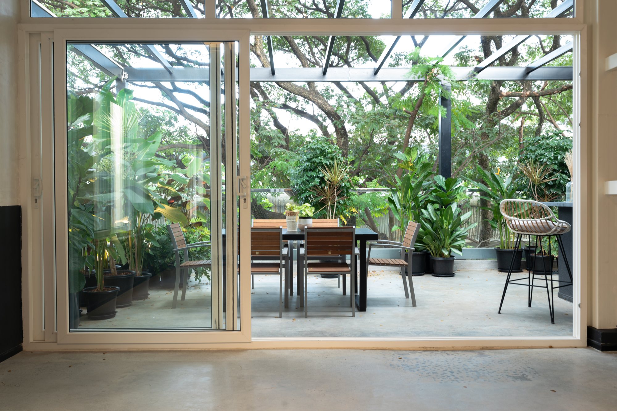 The terrace off the studio: sliding glass doors, potted plants, a table and chairs under trees.